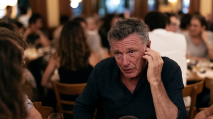 Homme d'une soixantaine d'années penché vers son interlocuteur dans un restaurant bondé