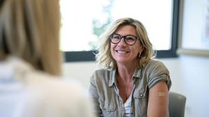 Femme souriante d'une soixantaine d'années, manche relevée et pansement au bras, dans l'espace de confidentialité d'une pharmacie